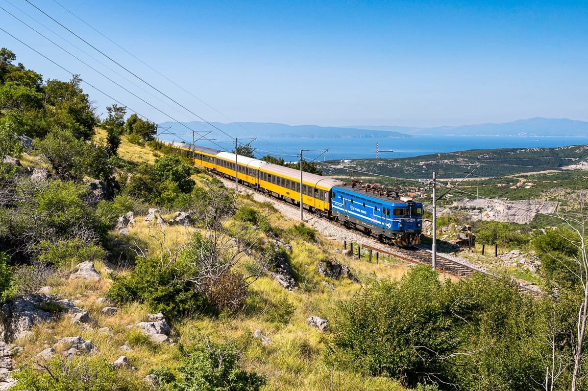 Ein gelber Nachtzug von RegioJet in einer kroatischen Küstenlandschaft