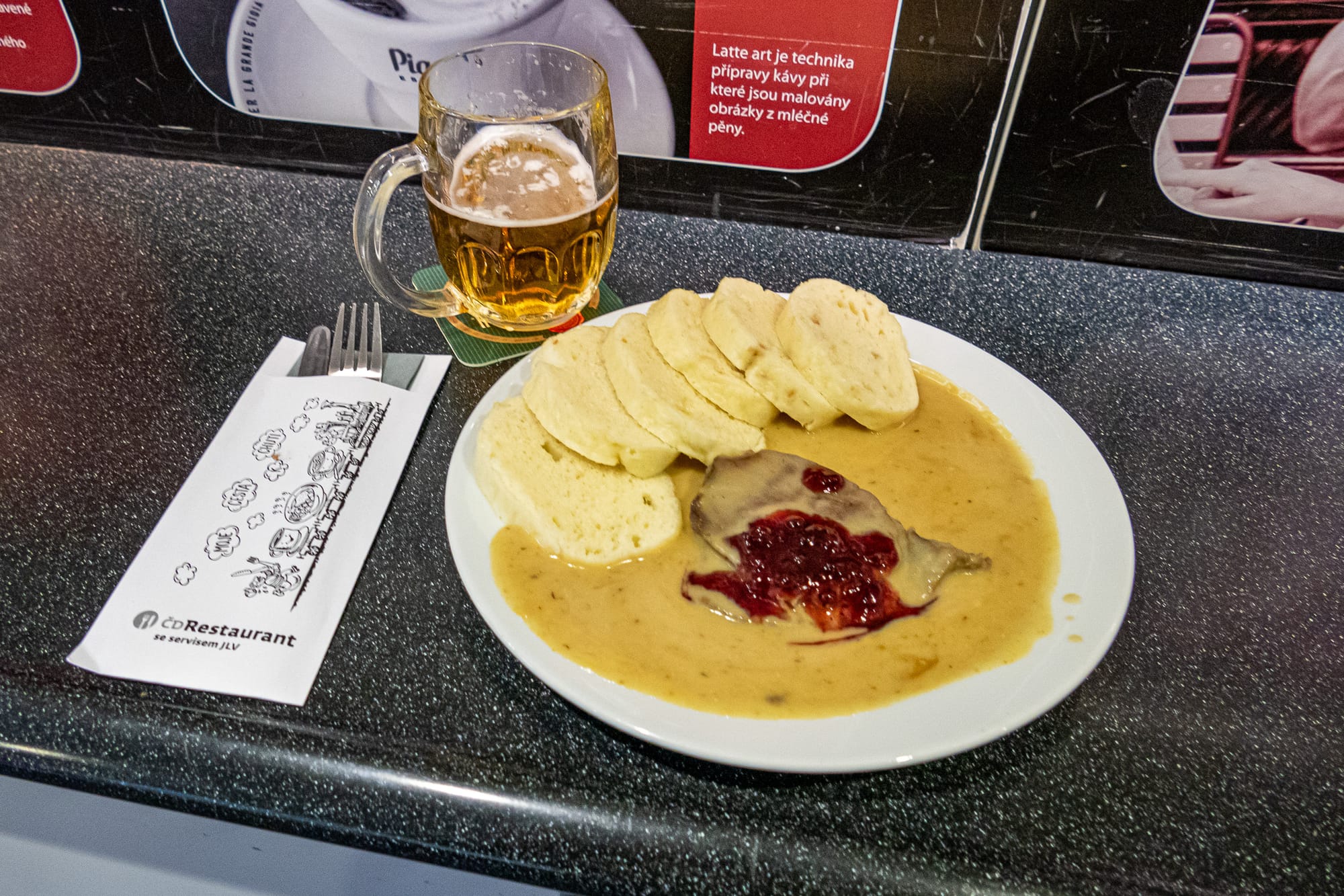 Ein Teller mit Lendenbraten, Knödeln und Rahmsauce, dazu ein Glas mit Bier