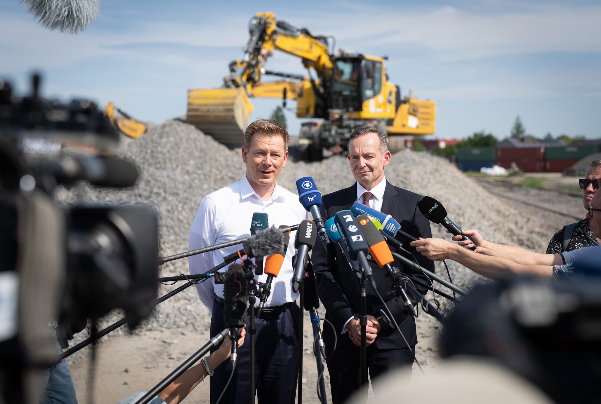 Volker Wissing und Bahnchef Lutz auf der Baustelle, von Mikrofonen umringt