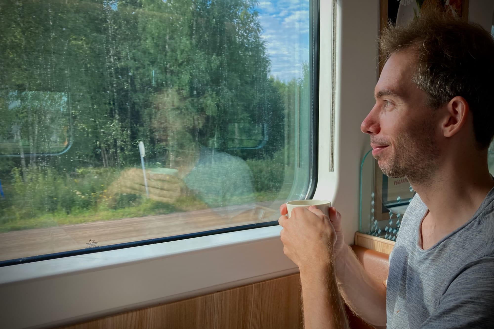 Ich schaue mit Kaffeetasse in der Hand bedeutungsvoll aus dem Zugfenster